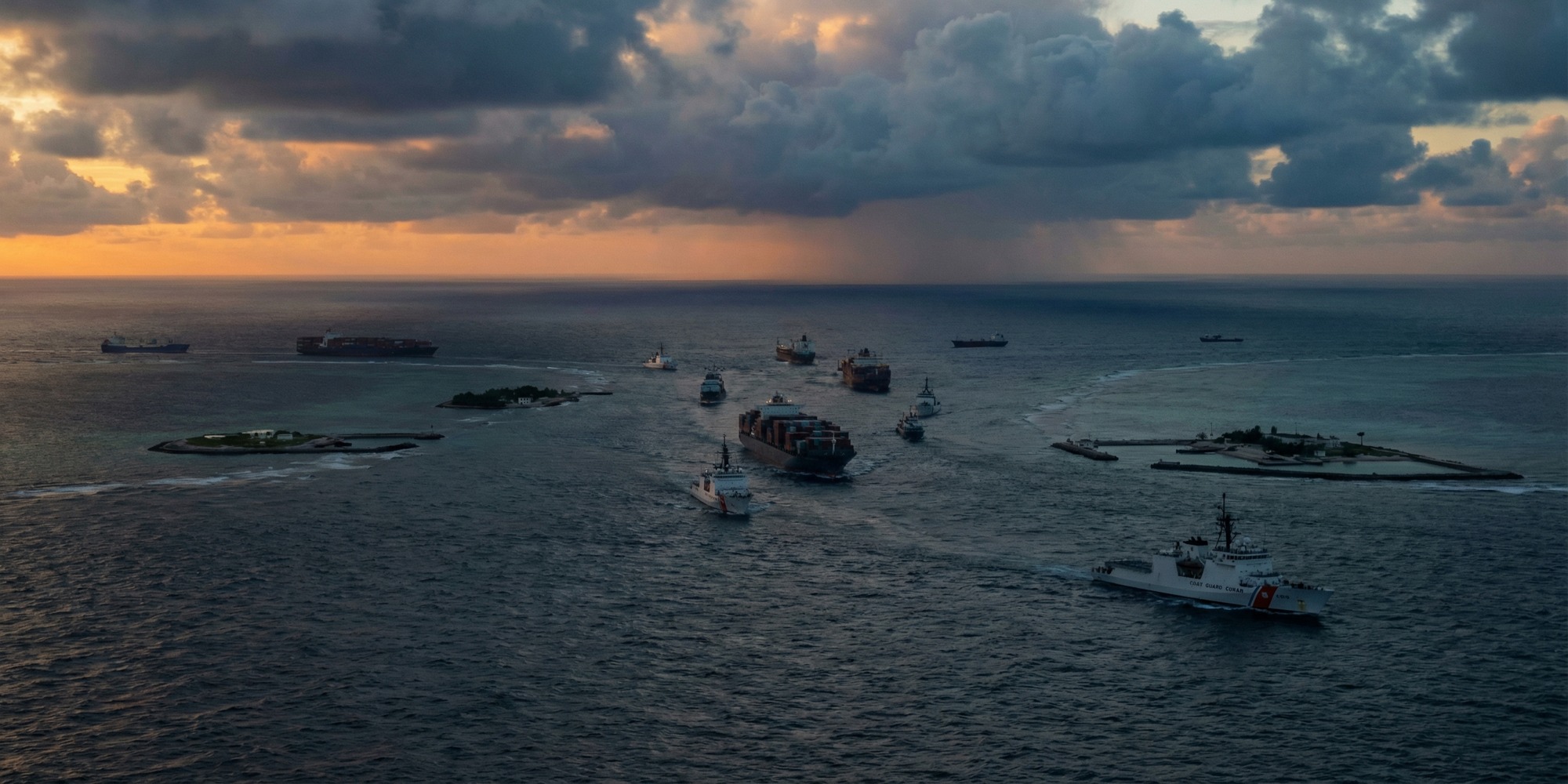 Aerial view of coast guard and cargo vessels navigating near a reef in the South China Sea under heavy dawn clouds