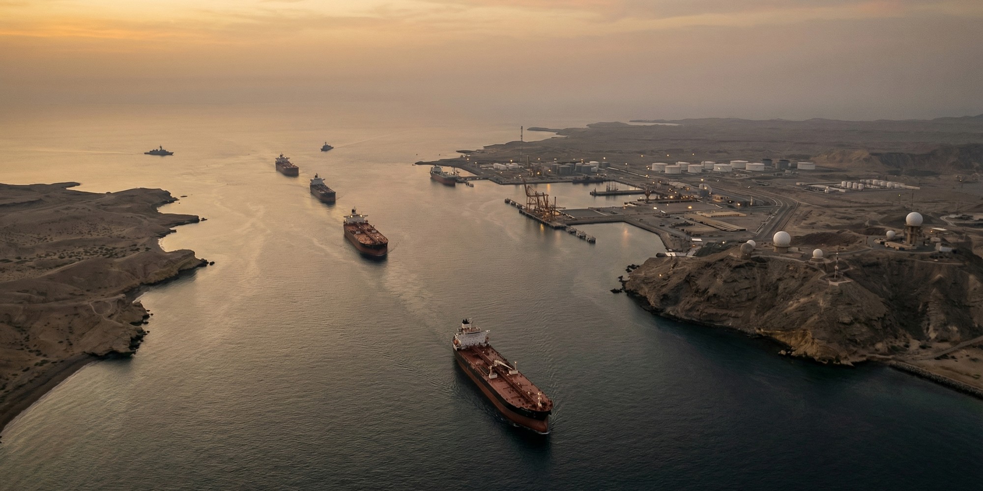 Aerial view of oil tankers transiting the Strait of Hormuz between rugged coastlines at dawn