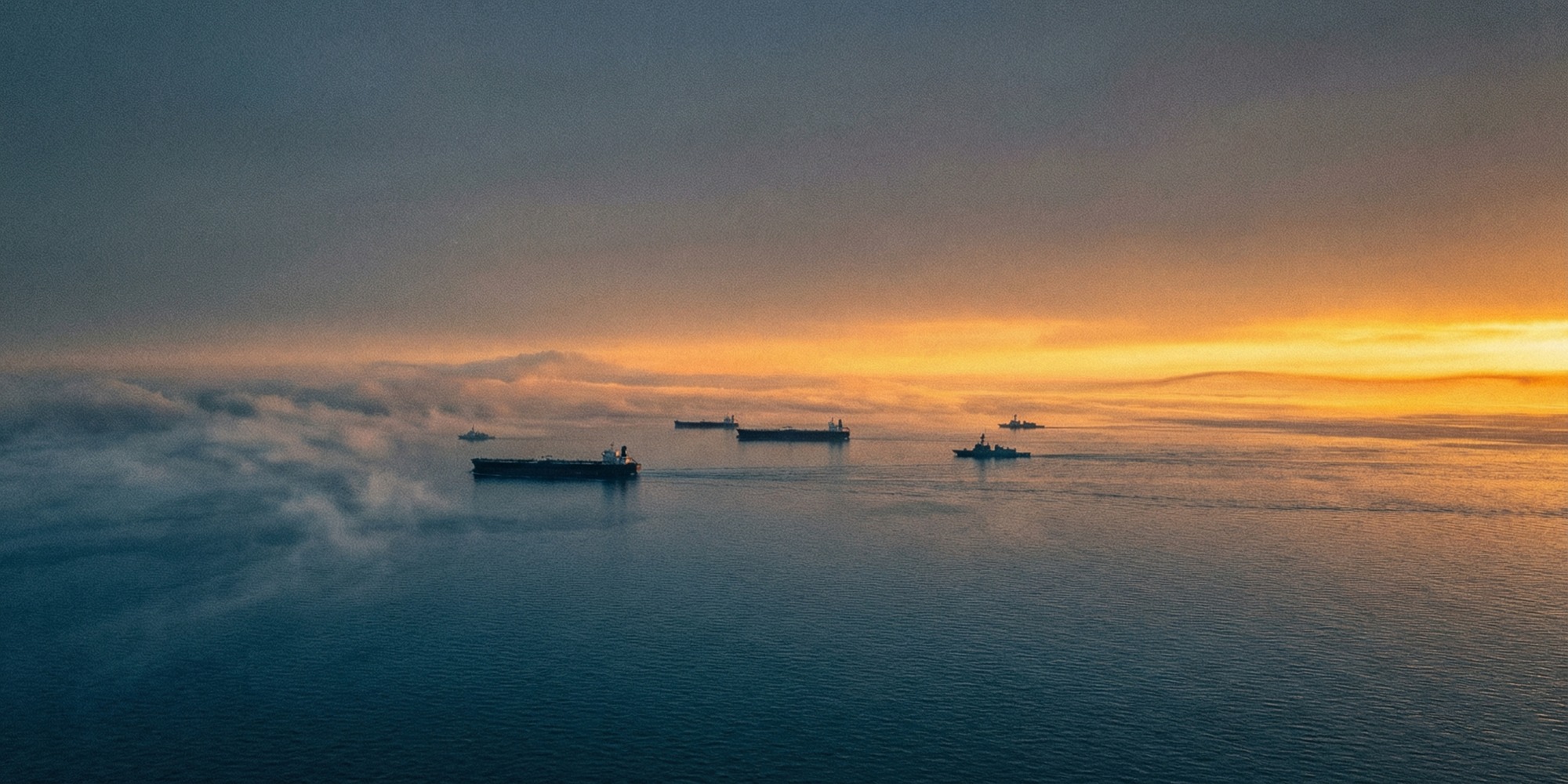 Aerial view of the Persian Gulf at dawn, oil tankers visible on calm waters under a golden horizon